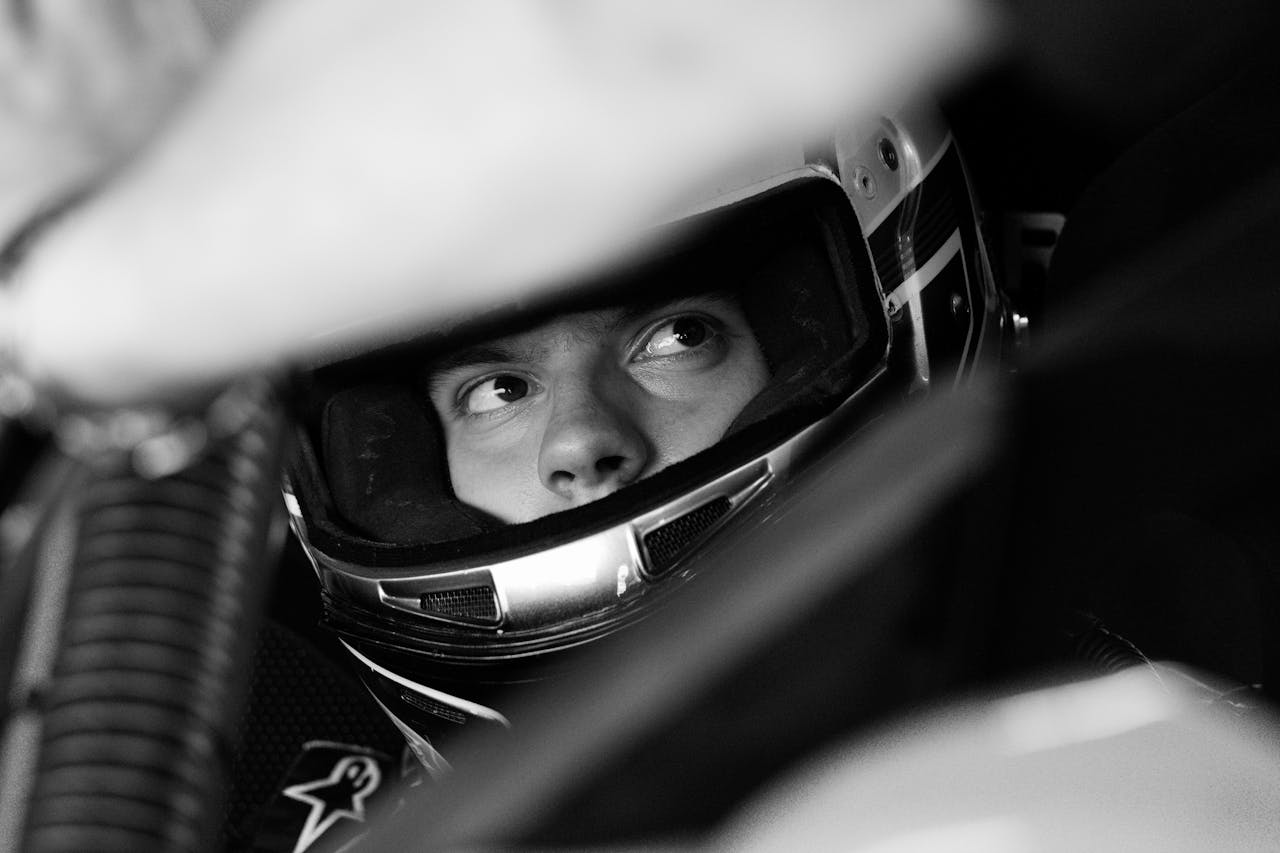Services Black and white photo of a race car driver intensely focused, wearing a helmet.