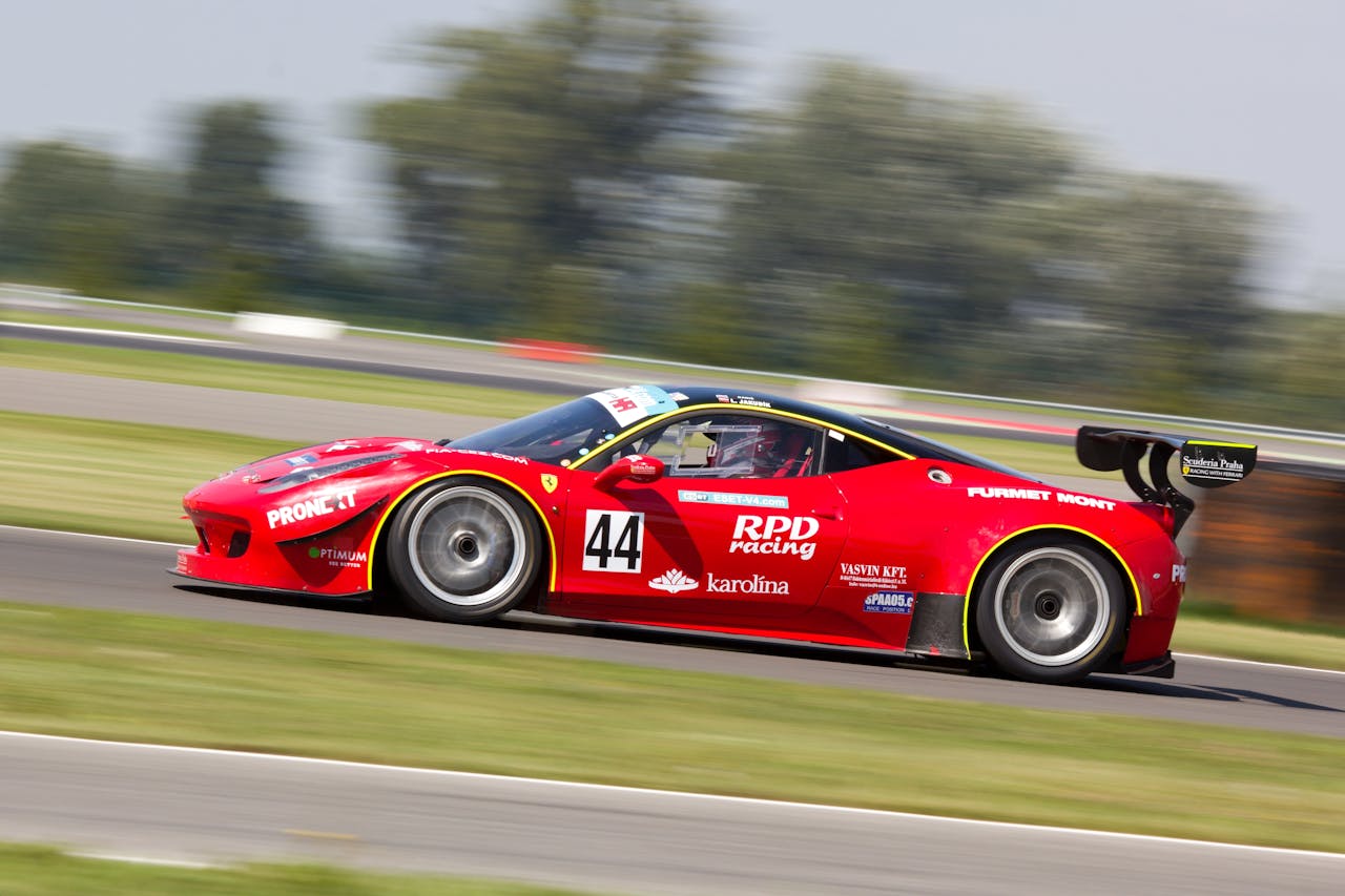 Services High-speed red race car in motion on track, captured in vibrant daylight.