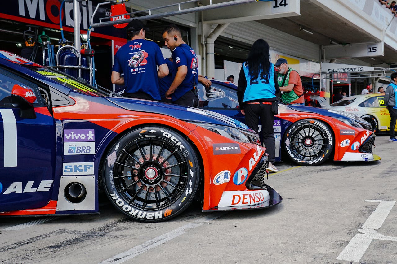 Home Close-up of colorful race cars in a pit stop with mechanics and crew preparing for a motorsport event.
